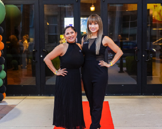 two women posing standing on a red carpet